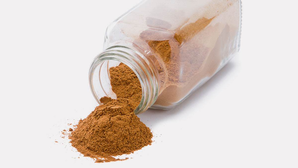 Ground cinnamon spilling from spice jar isolated on white background.
