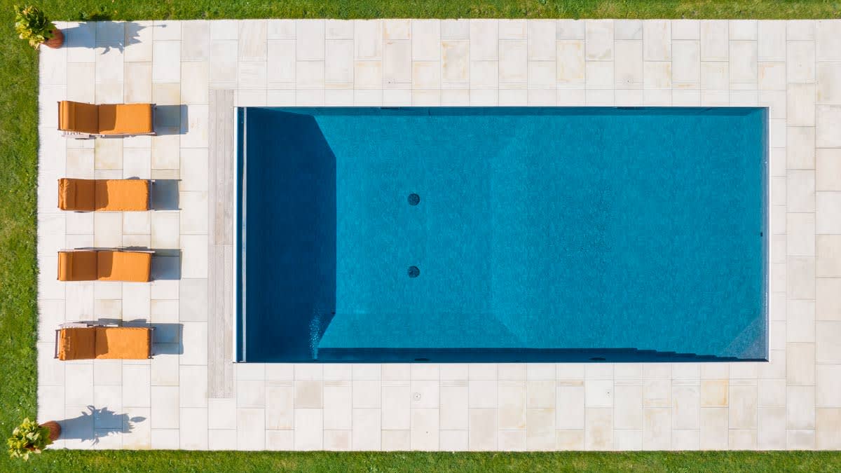 overhead view of pool with stone patio, 4 orange lounge chairs, and grass along outer edge