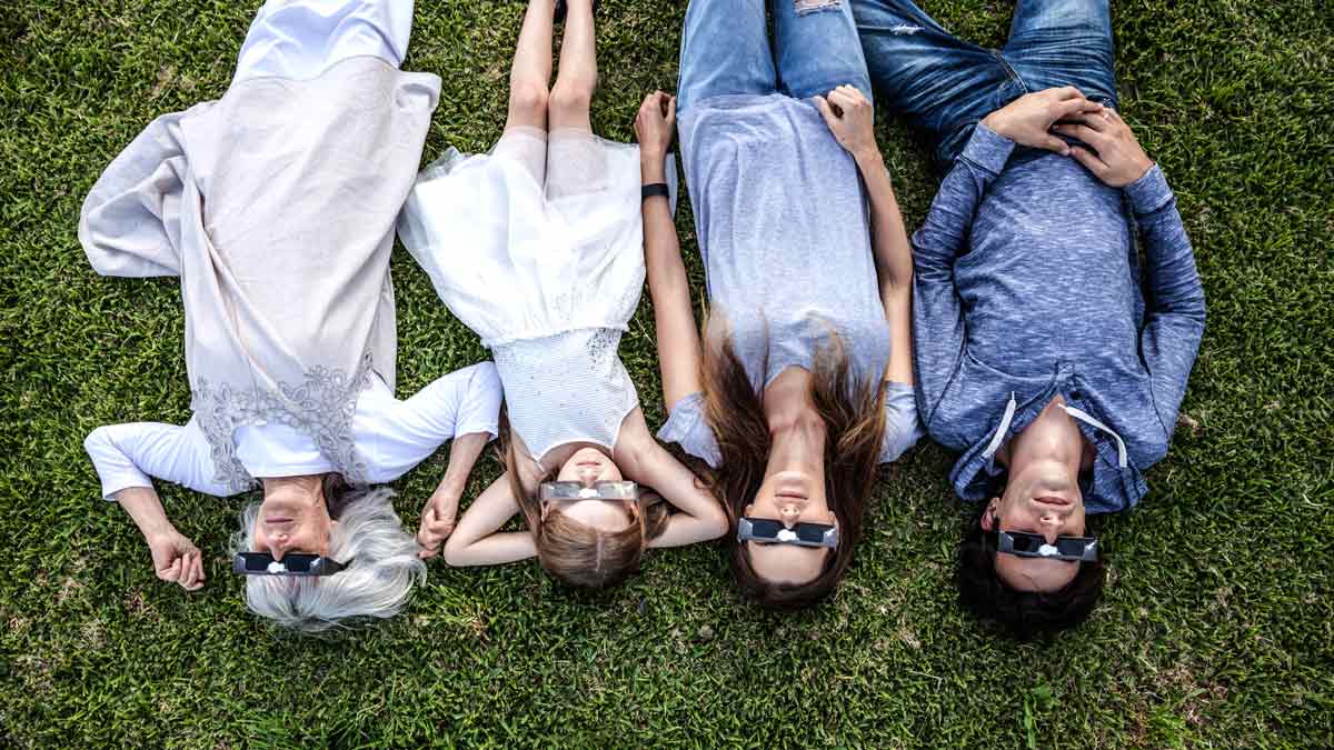 overhead view of family lying on grass with solar eclipse glasses