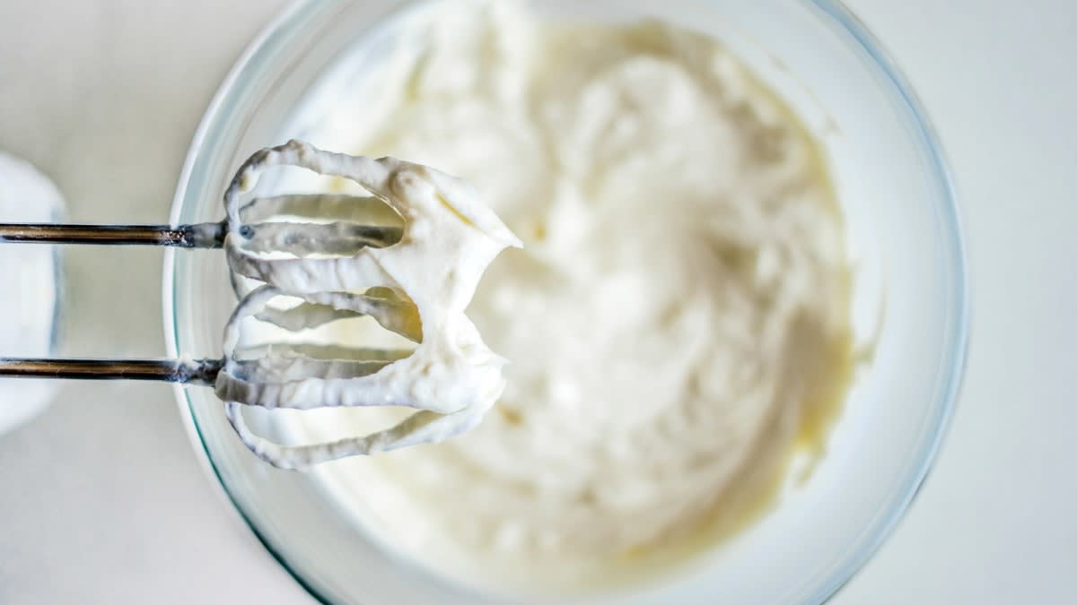 close up overhead view of hand mixer whisks with whipped cream above bowl of whipped cream