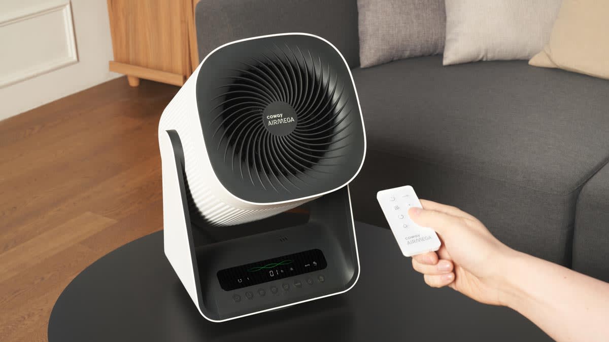 A person using a remote control to turn on a Coway Airmega Aim air purifier.