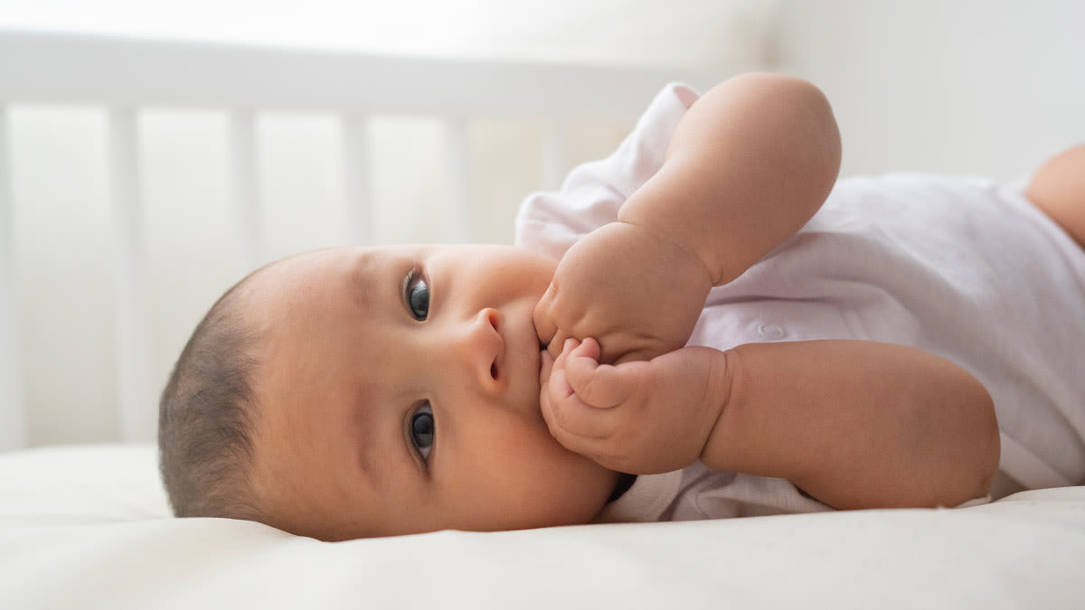 Baby on laying in crib on back with hand in mouth
