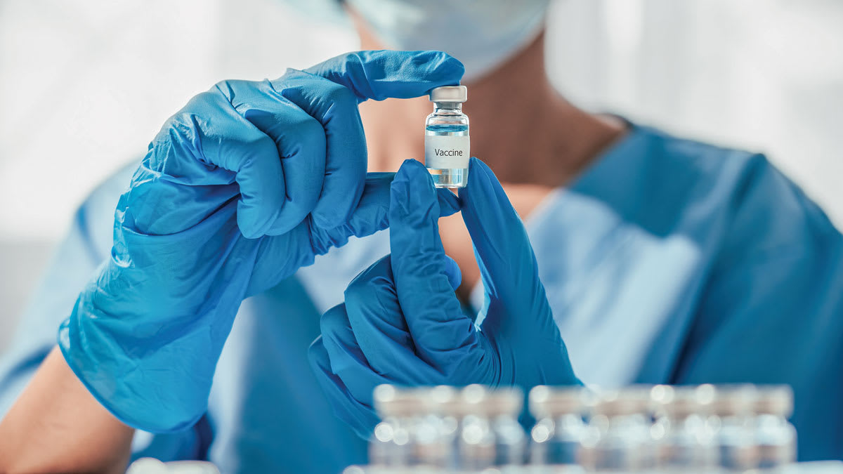close up of person's hands holding glass vaccine vile, wearing blue surgical gloves and scrubs