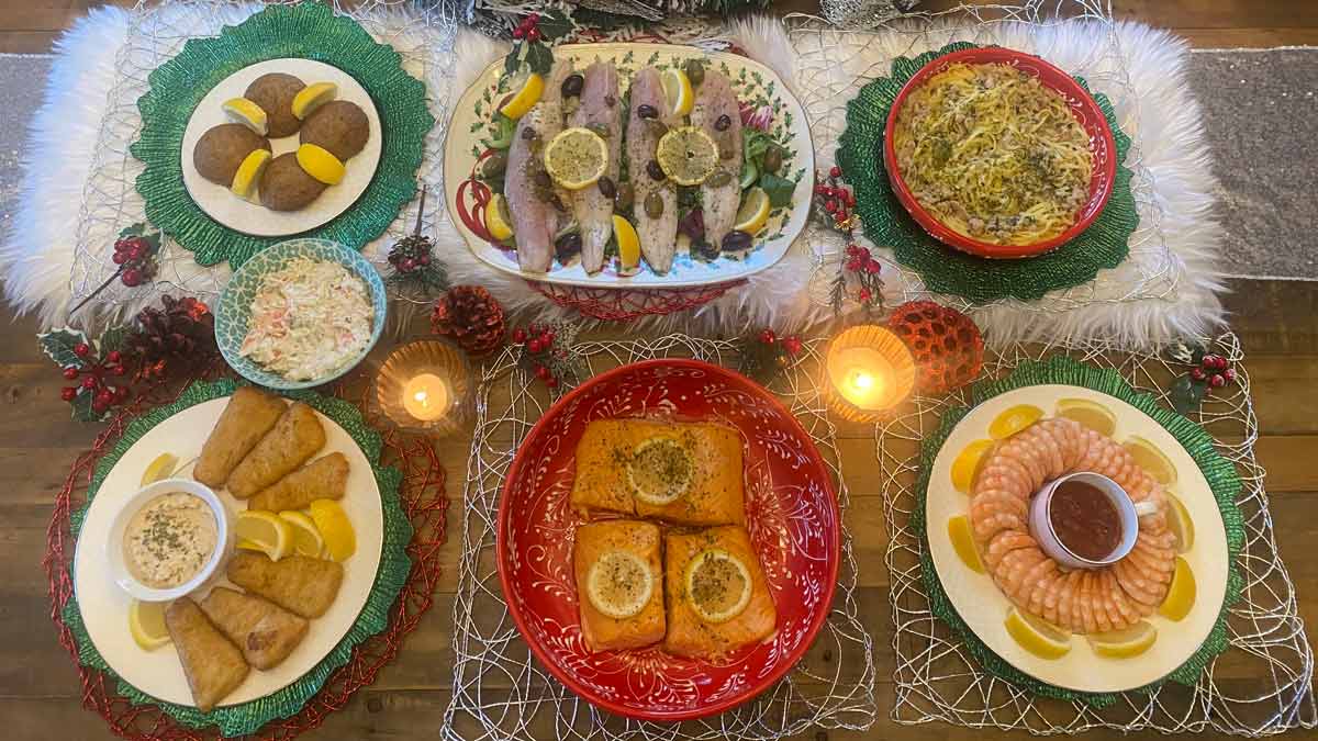 overhead view showing the seven dishes served during the Feast of Seven Fishes with lit candles and other holiday decor