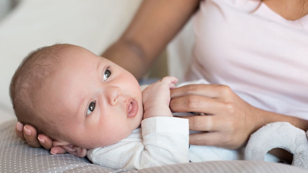 A mother holding her newborn baby's head while it rests on a nursing pillow.