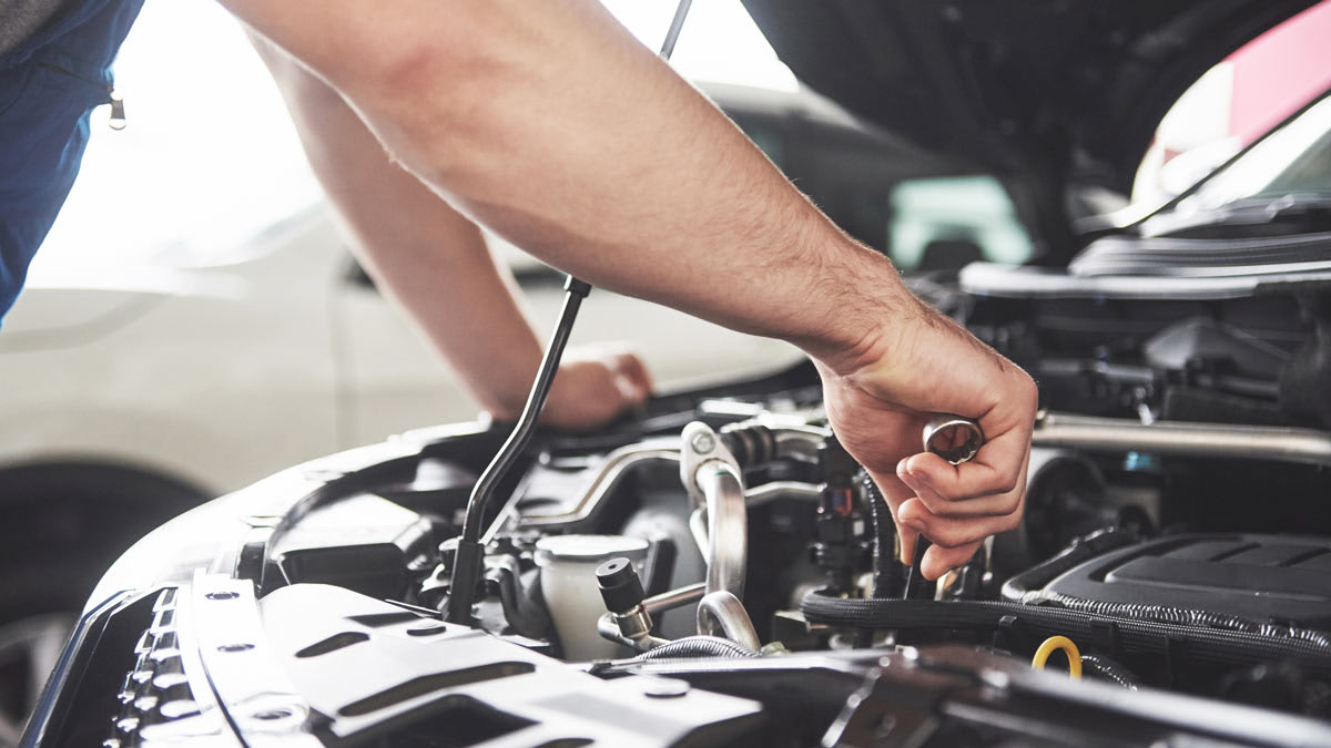 close up of person using wrench under hood of car