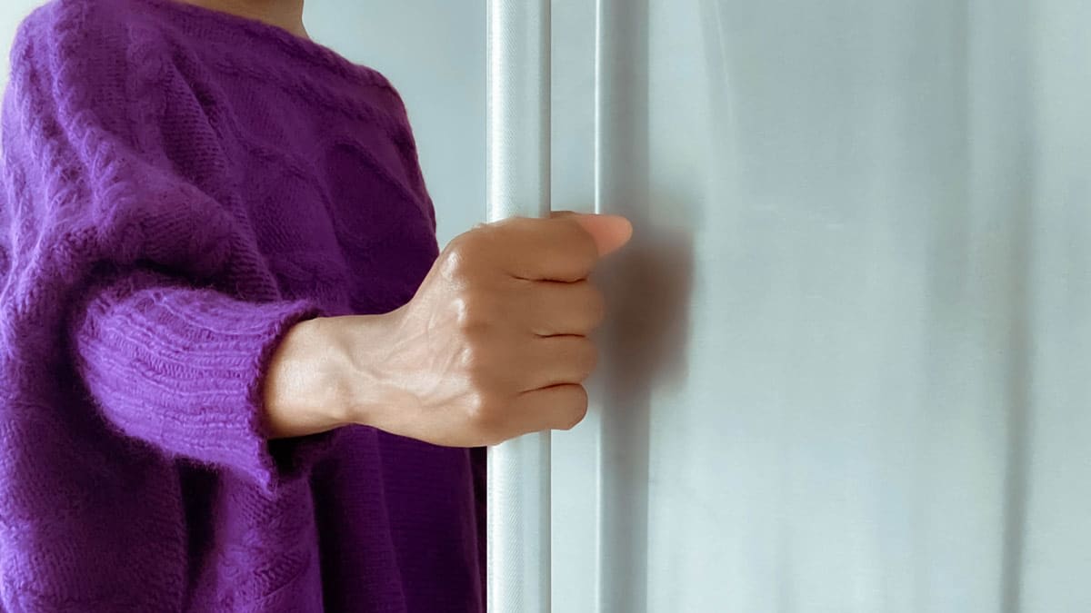 detail of person in purple sweater holding refrigerator handle to a stainless steel refrigerator