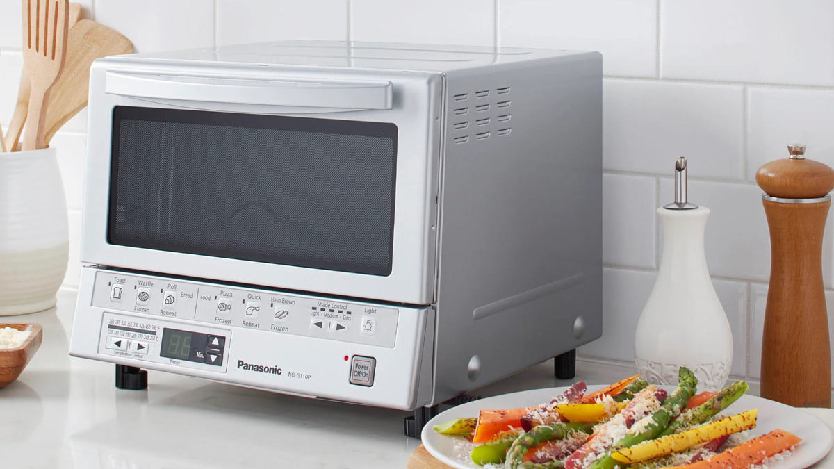 Panasonic FlashXpress NB-G110P microwave on white countertop with white subway tile backsplash, plate of roasted vegetables with cheese to right of microwave