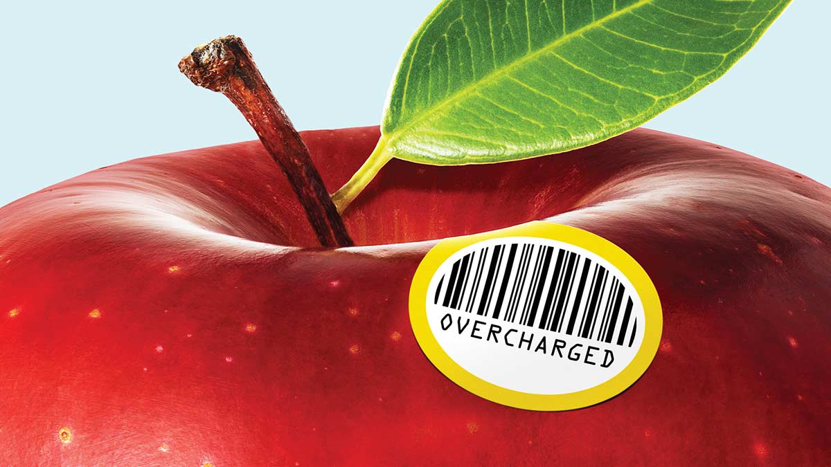 A close-up of a red apple that features a barcode sticker that conspicuously displays "OVERCHARGED"