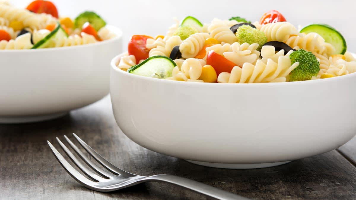 Bowl of pasta salad with vegetables on a table.