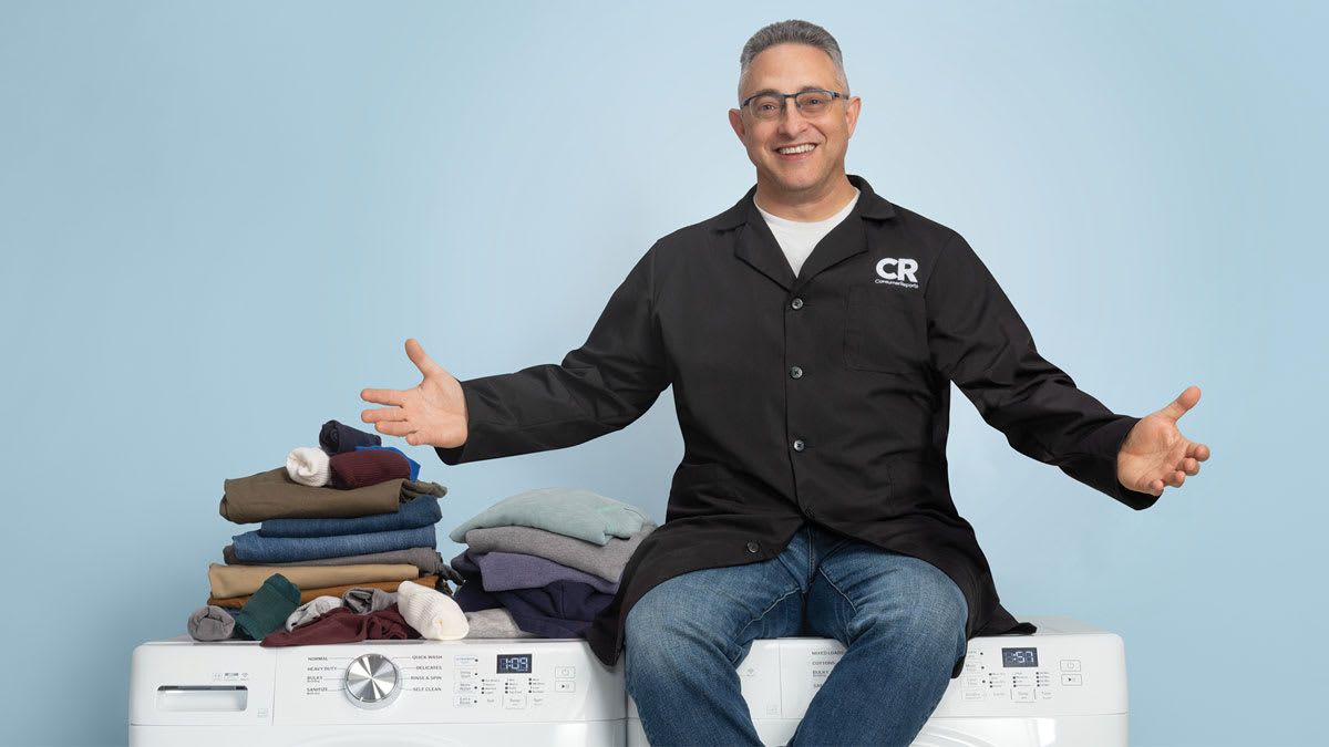 Laundry expert Rich Handel sitting on top of a top-rated washer and dryer, surrounded by clean folded laundry looking happy to explain how to get your clothes really clean.