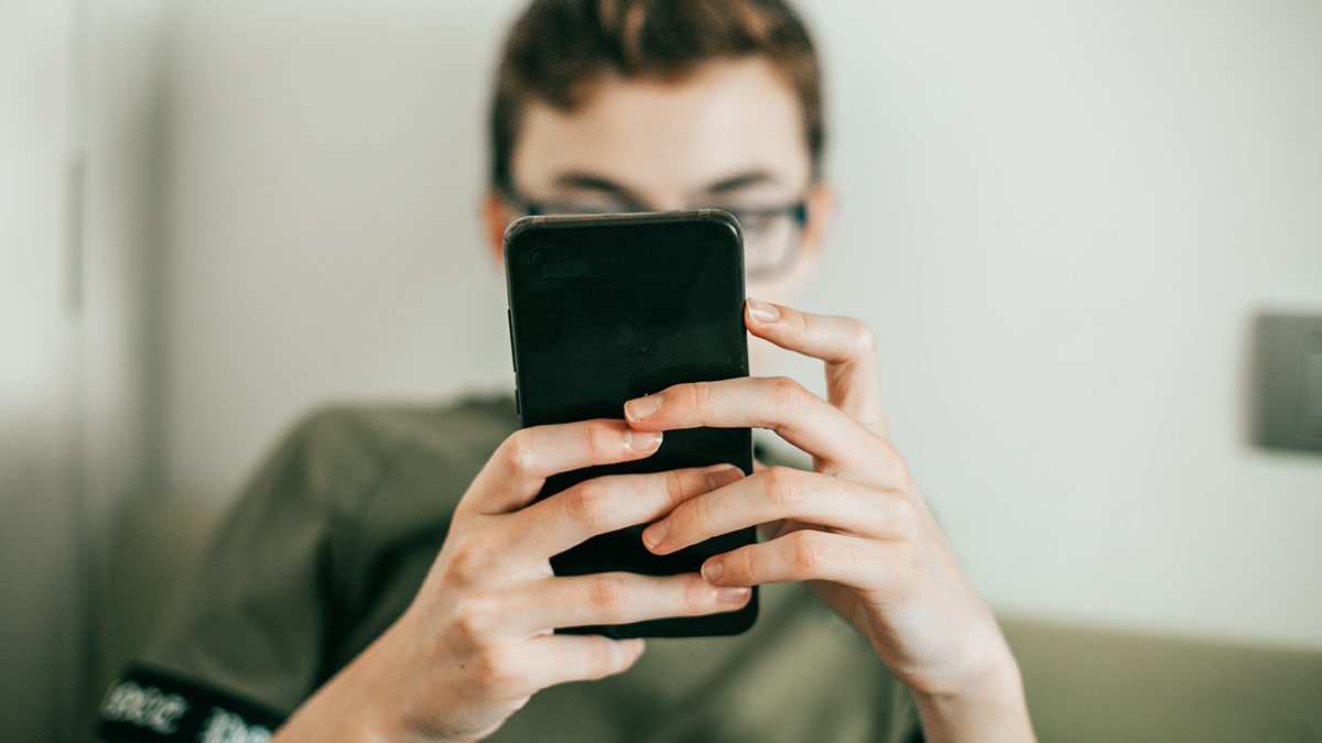 Teenager looking at their cell phone with the phone covering their face.