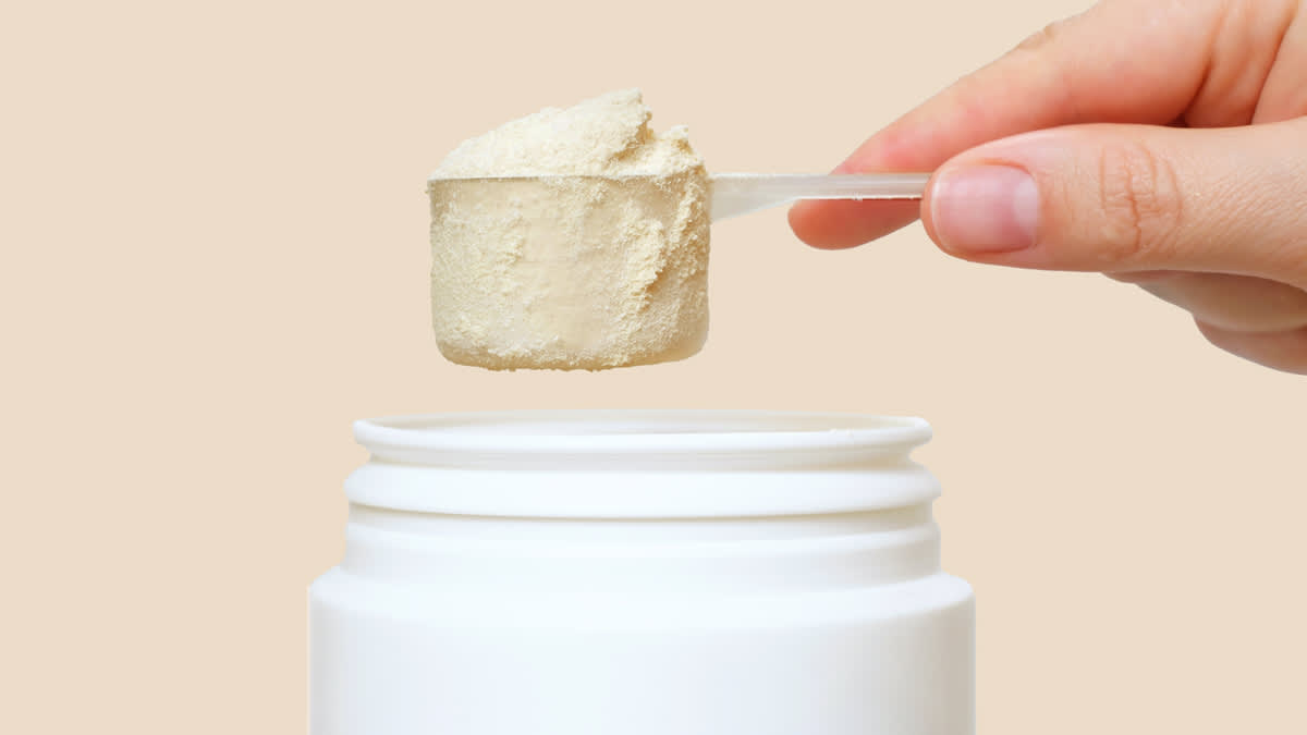 Hand holding protein powder scoop over container