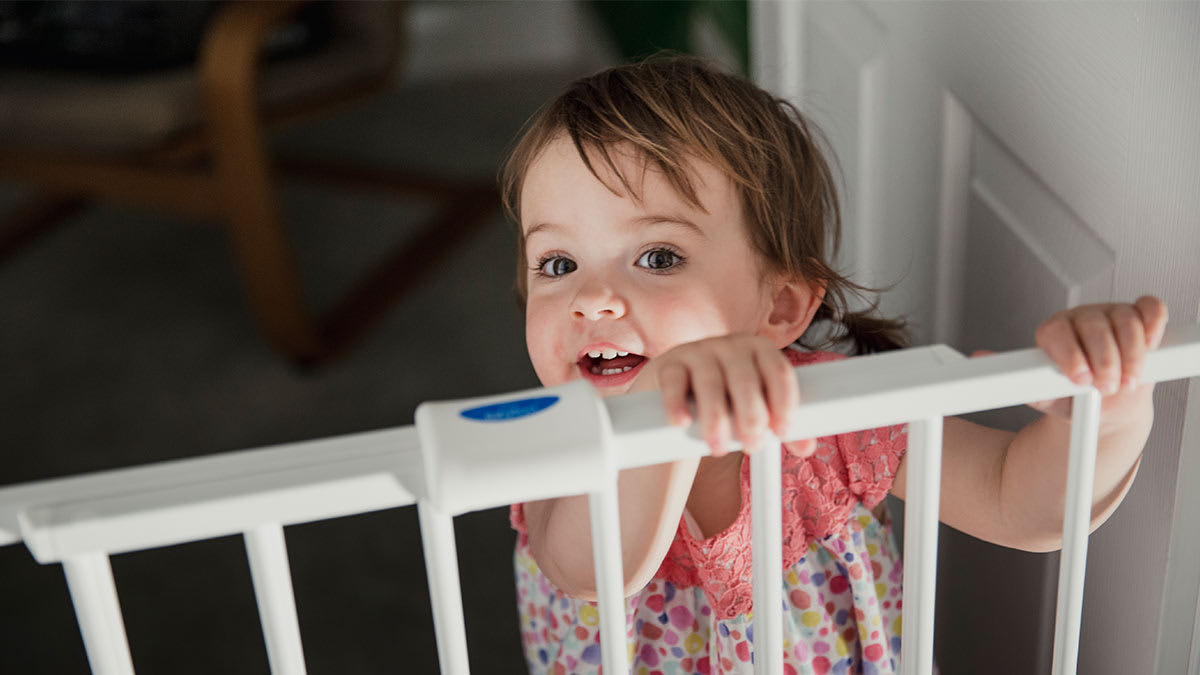 Toddler looking up and smiling over a baby gate.