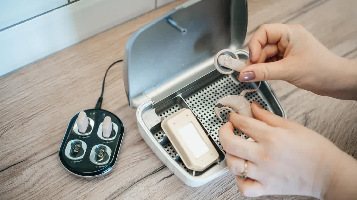 person holding cochlear implant above hearing aid cleaning kit with battery charging dock next to cleaning kit