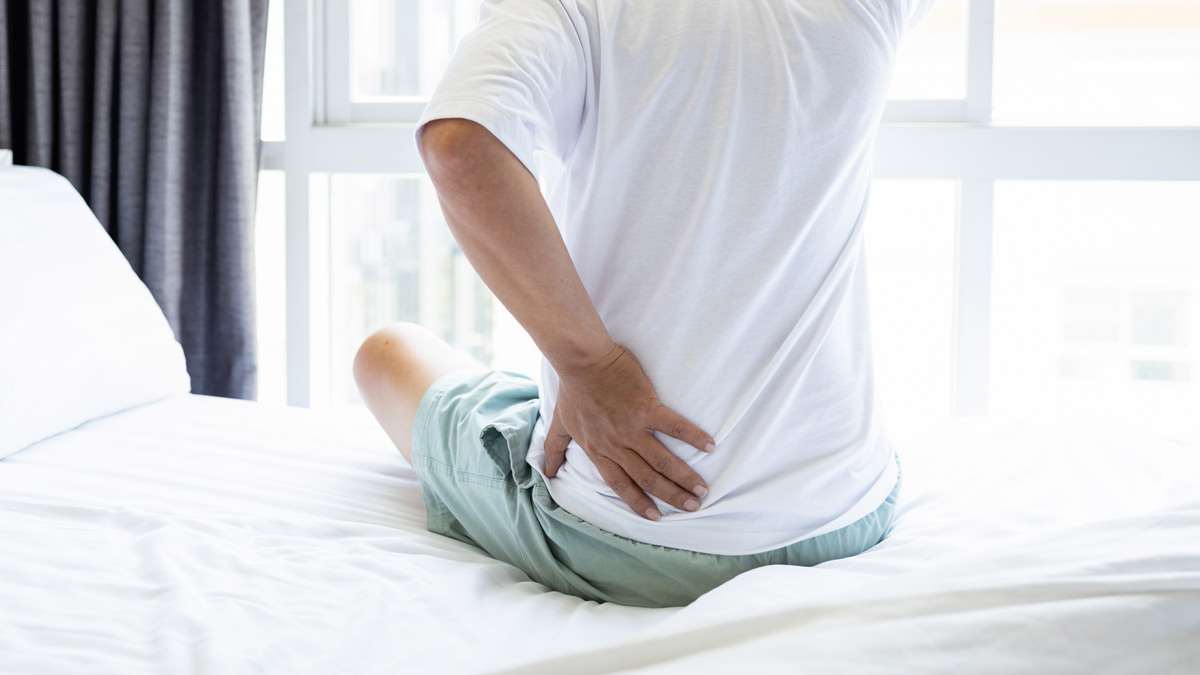 detail of person sitting on edge of bed with hand on their hip as though in pain