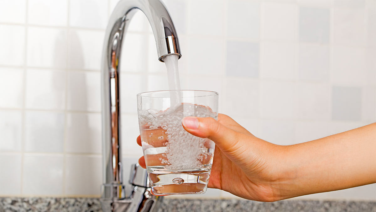 Hand holding a glass under a flowing kitchen tap.