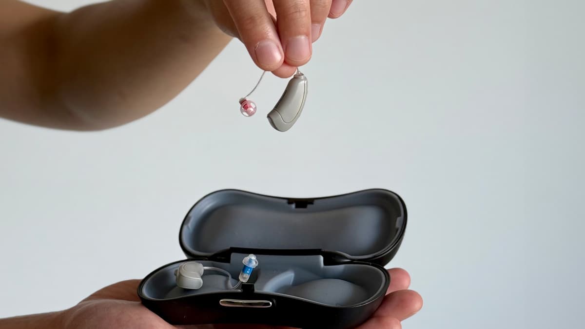 detail of hand holding Concha Sol hearing aid over case with the other hearing aid