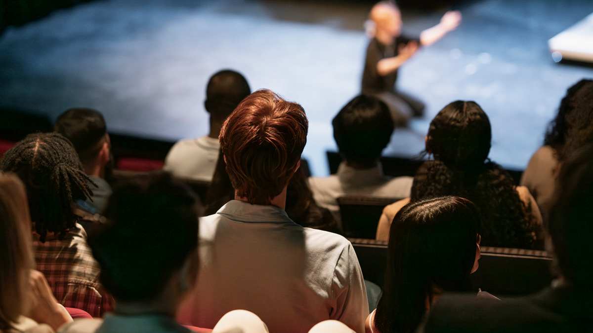 backs of people in audience looking at stage with performer during a play