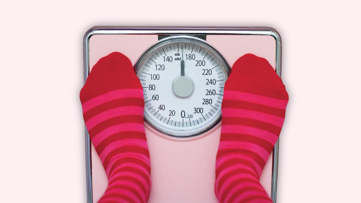 overhead view of feet with pink and red striped socks on scale that says "uh oh!", pink background
