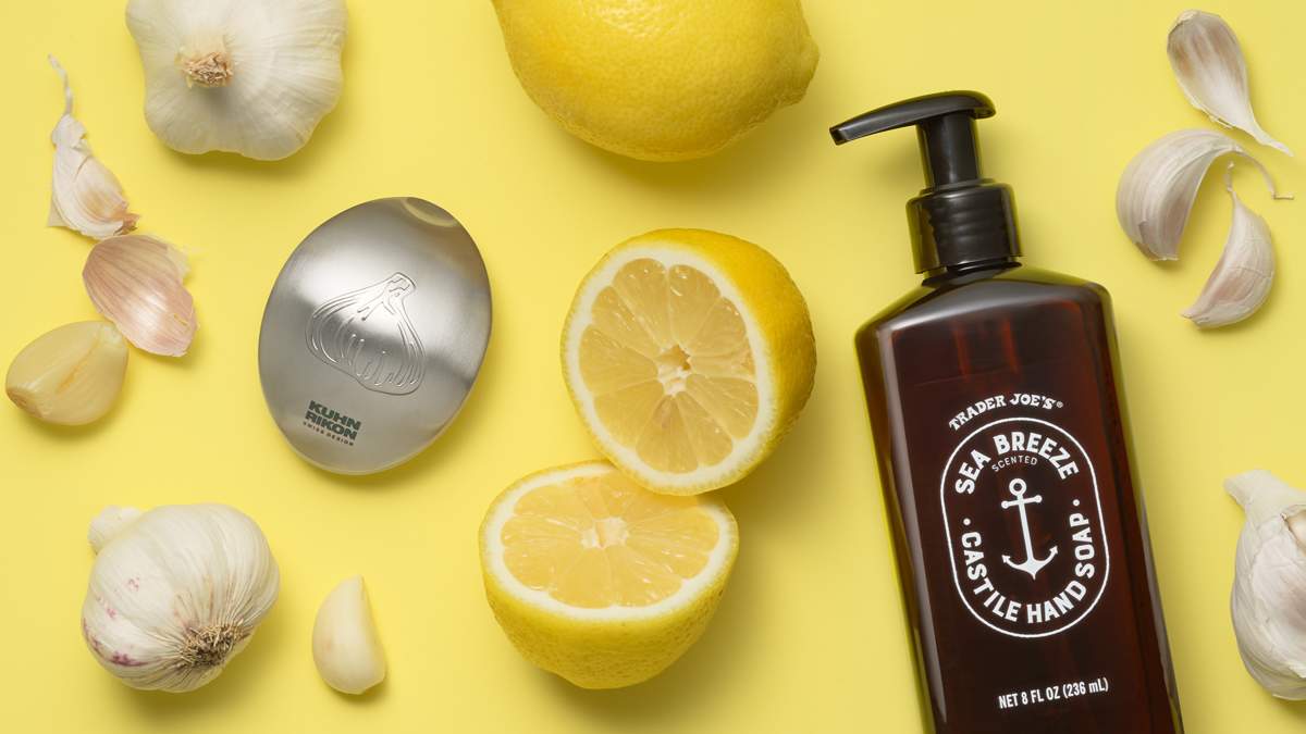 Garlic bulbs and cloves, halved lemons, a stainless steel odor-removing soap bar, and a bottle of Trader Joe’s Sea Breeze castile hand soap on a yellow background.