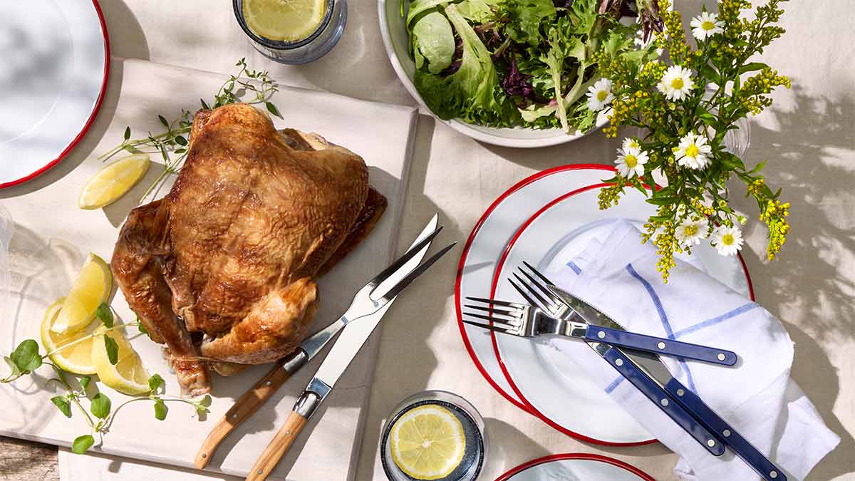Rotisserie chicken on a cutting board served in a picnic setting with salad, lemon water, and red-rimmed plates.