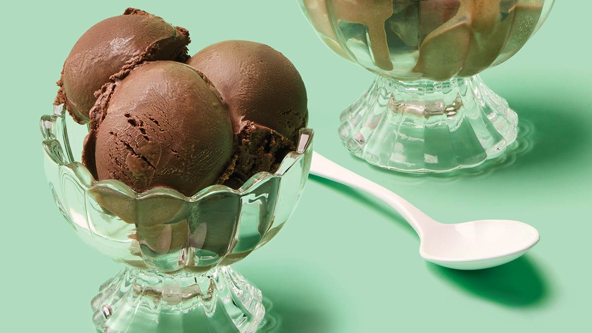 Scoops of chocolate ice cream in glass bowls beside a white spoon.