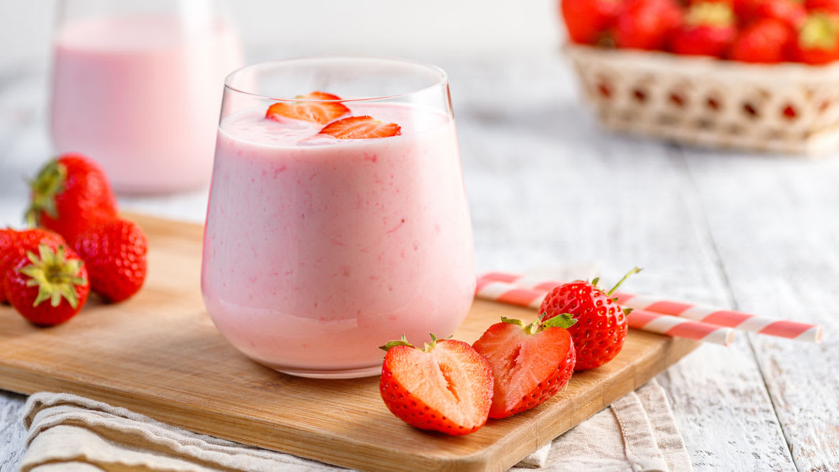 A strawberry smoothie on a cutting board with strawberries and straws.