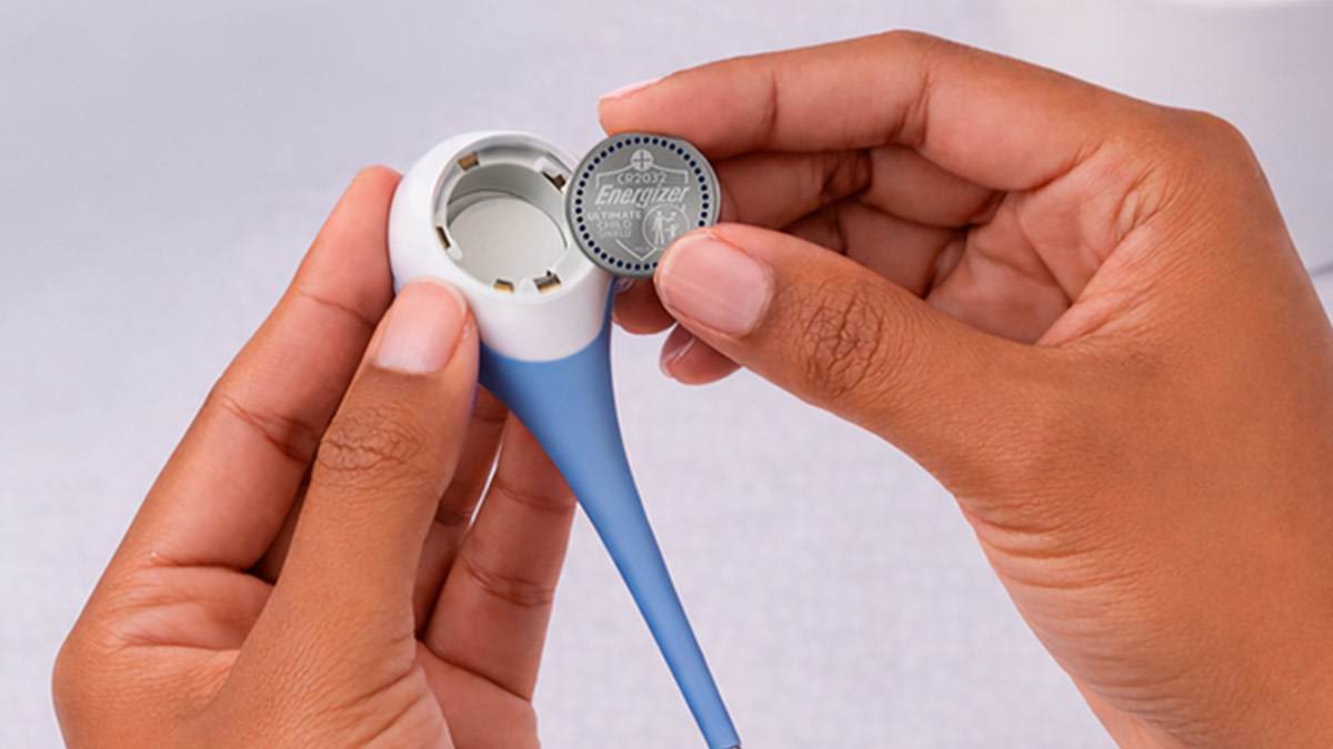 Hands placing the Energizer button battery into a thermometer.