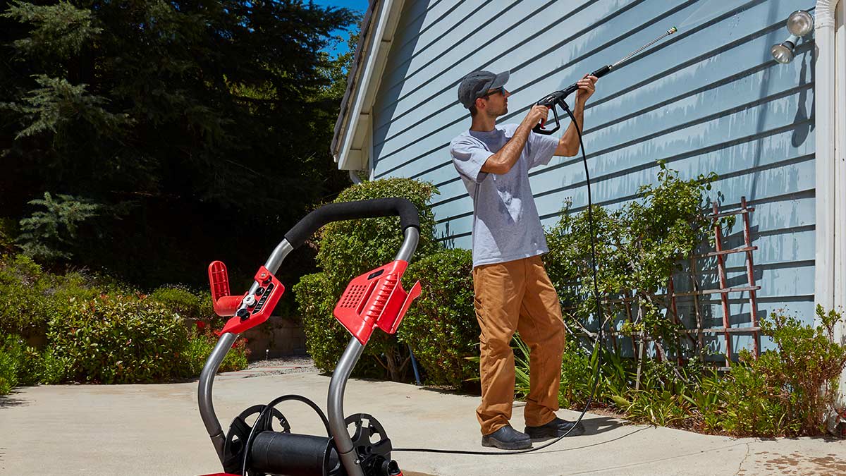 A man using a Bauer pressure washer to clean the siding on a house.