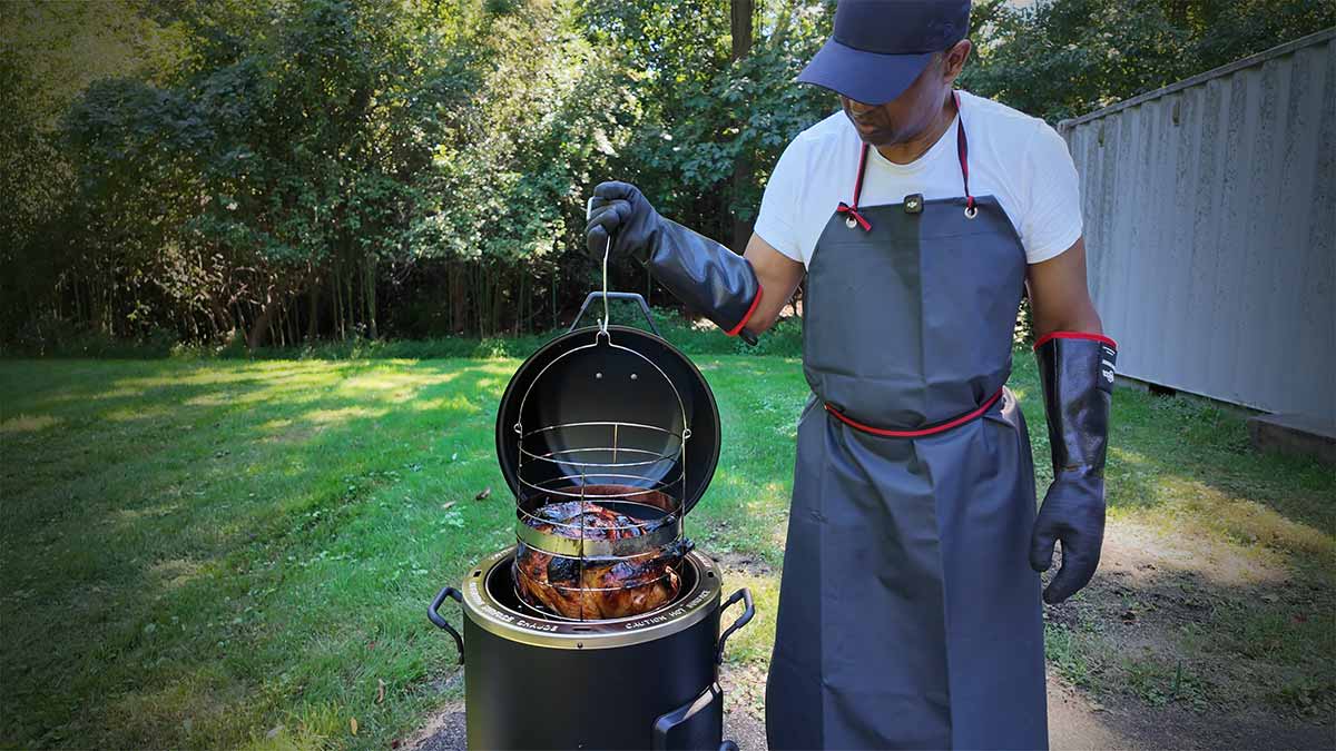 person wearing rubber cloves and apron while removing deep fried turkey from outdoor fryer