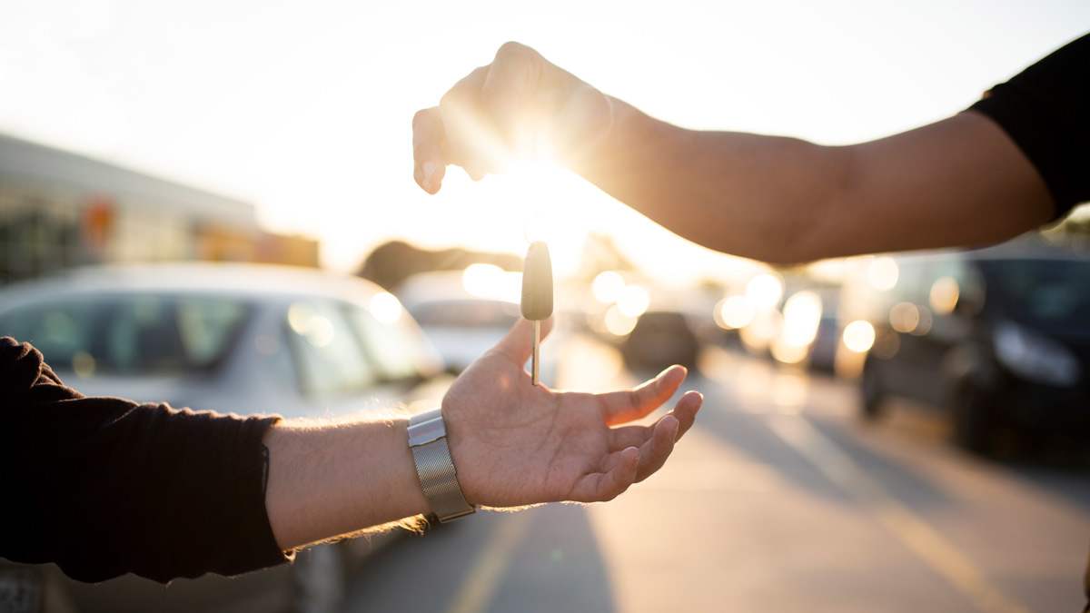 A person handing over a car key to another person in a parking lot.