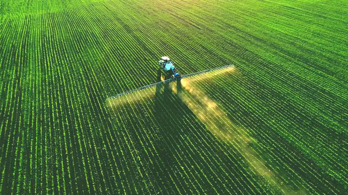 high angle view of tractor spraying fertilizer on green field