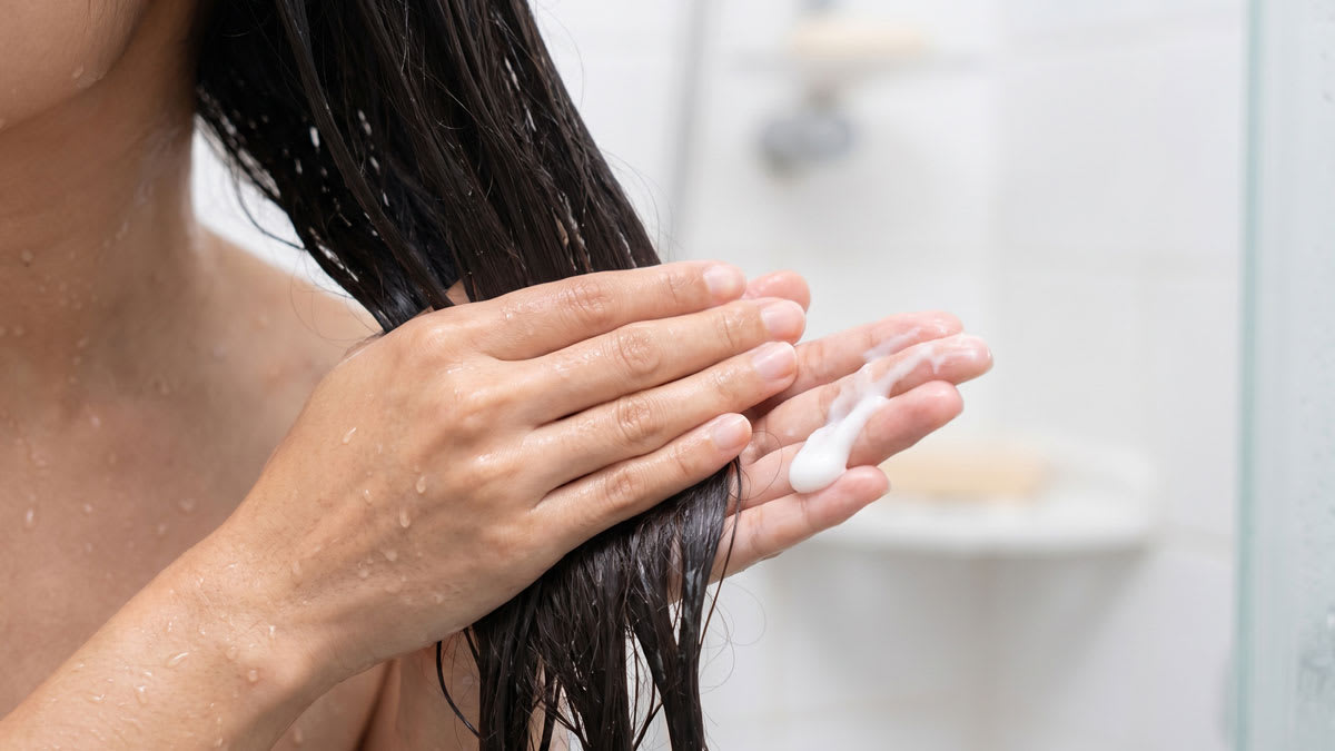 Woman rubbing hair conditioner into wet hair in the shower