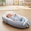 A baby asleep on their back in a Sunlove Premium Cotton Baby Lounger Nest thats sitting on the floor.