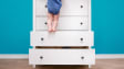 Toddler baby climbed up on the open chest of drawers
