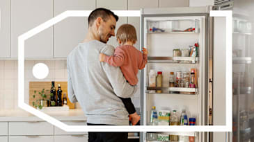 Parent holding a young child next to an open refrigerator.