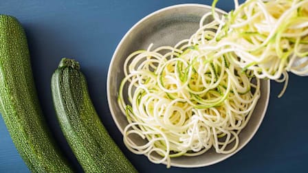 overhead view of zucchini spirals in bowl with 2 zucchini next to bowl
