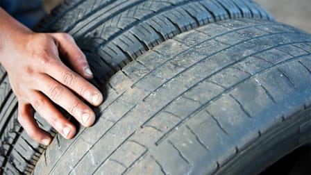 A person inspecting the tread on a worn tire.