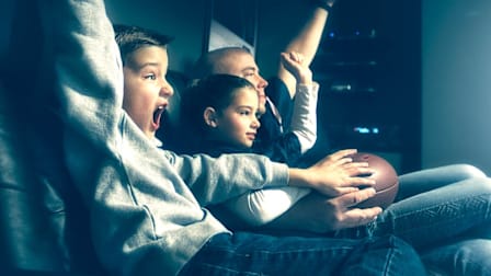 Family sitting on couch watching football on TV.