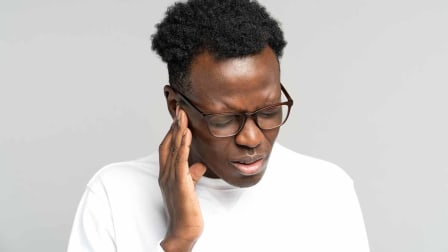 person in visible pain holding hand to ear