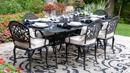 An outdoor table set for a meal sits on top of an outdoor rug