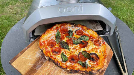 A finished pizza being slid out of the Ooni Pizza Oven on a wooden pizza peel