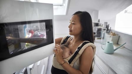 mother with baby in baby carrier putting food in microwave