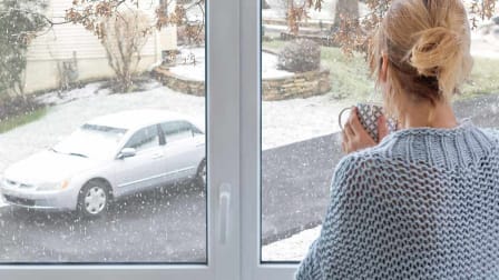 Woman looking out window at car covered in snow