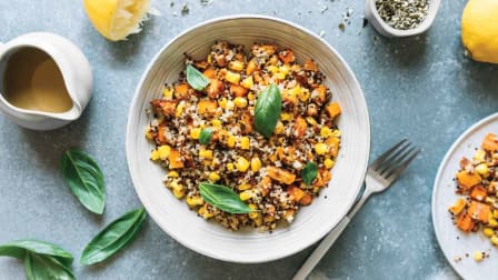 overhead view of bowl with grains and vegetables with basil, fork and lemon on surface