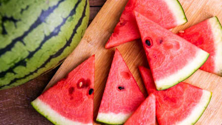 sliced triangles of watermelon on a cutting board with a whole watermelon next to it