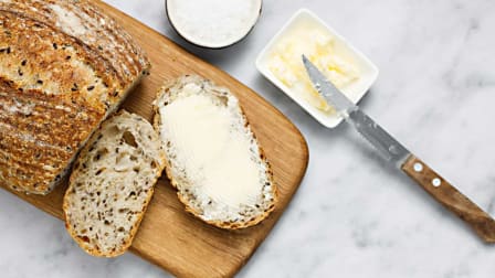 overhead view of loaf of bread with 2 slices on cutting board and butter with knife next to bread