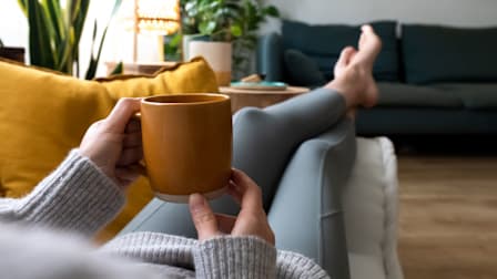 Woman relaxing at home with cup of coffee lying on couch