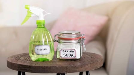 end table in front of couch with green spray bottle of vinegar and jar with baking soda